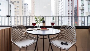 A balcony with two wicker chairs, a round table, a bottle of wine, and a glass of red wine. - Next Paulista by Viva - Apartamentos completos ao lado da Av Paulista e MASP (São Paulo)
