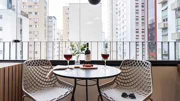 Uma varanda com duas cadeiras de vime, uma mesa redonda, uma garrafa de vinho e um copo de vinho tinto.