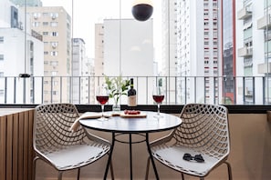 A balcony with two wicker chairs, a round table, a bottle of wine, and a glass of red wine.