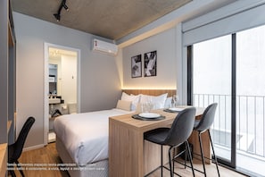 Une chambre d’hôtel avec un lit, un bureau avec des chaises, un balcon et des œuvres d’art au mur.