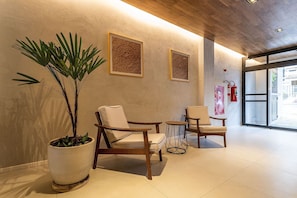 A lobby with three wooden chairs, a large potted plant, and two framed artworks on the wall.