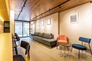 A modern interior with a wooden ceiling, a grey sofa, orange and blue chairs, and a dining table.