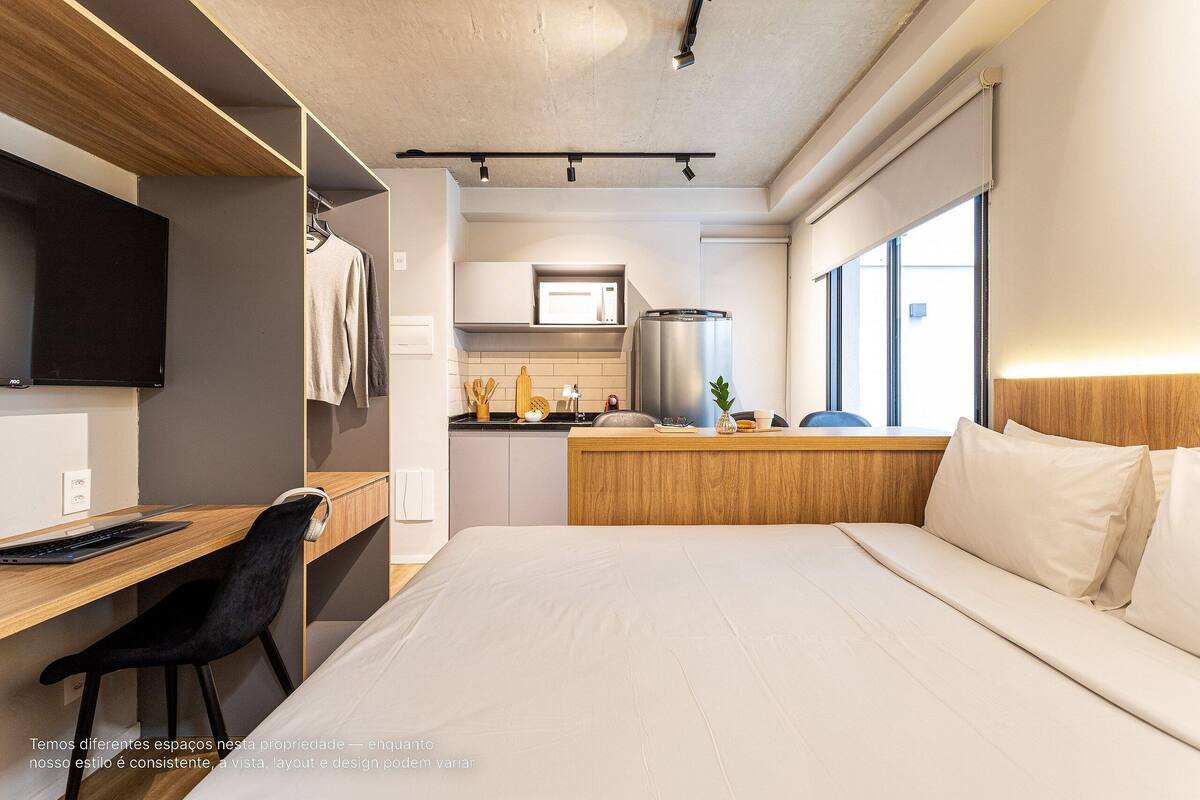 Une chambre d’hôtel moderne avec un bureau en bois, une chaise noire et un lit avec une literie blanche.
