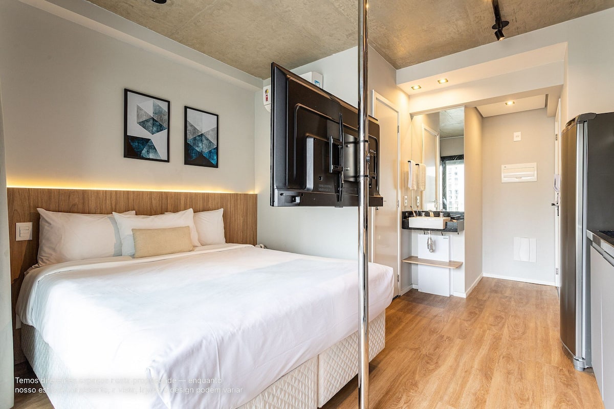 Une chambre d’hôtel moderne dotée d’un grand lit, d’un téléviseur intégré, d’un coin cuisine et offrant une vue sur la ville.
