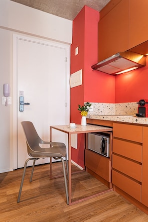 Una cocina compacta con horno integrado, cafetera y una pequeña mesa con una silla.