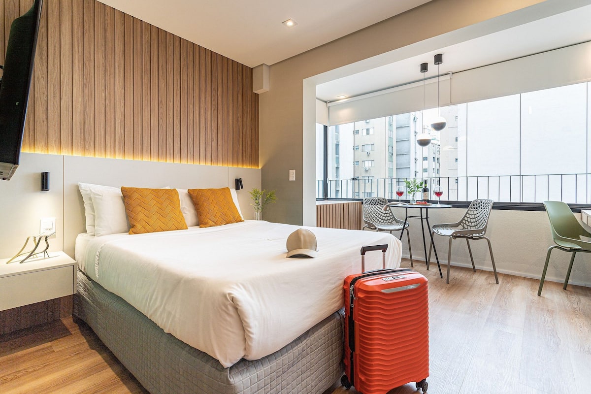 Une chambre d’hôtel avec un lit, une petite table, des chaises, un balcon avec vue et une valise.