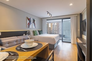 A modern hotel room with a sofa, dining table, and a bed.
