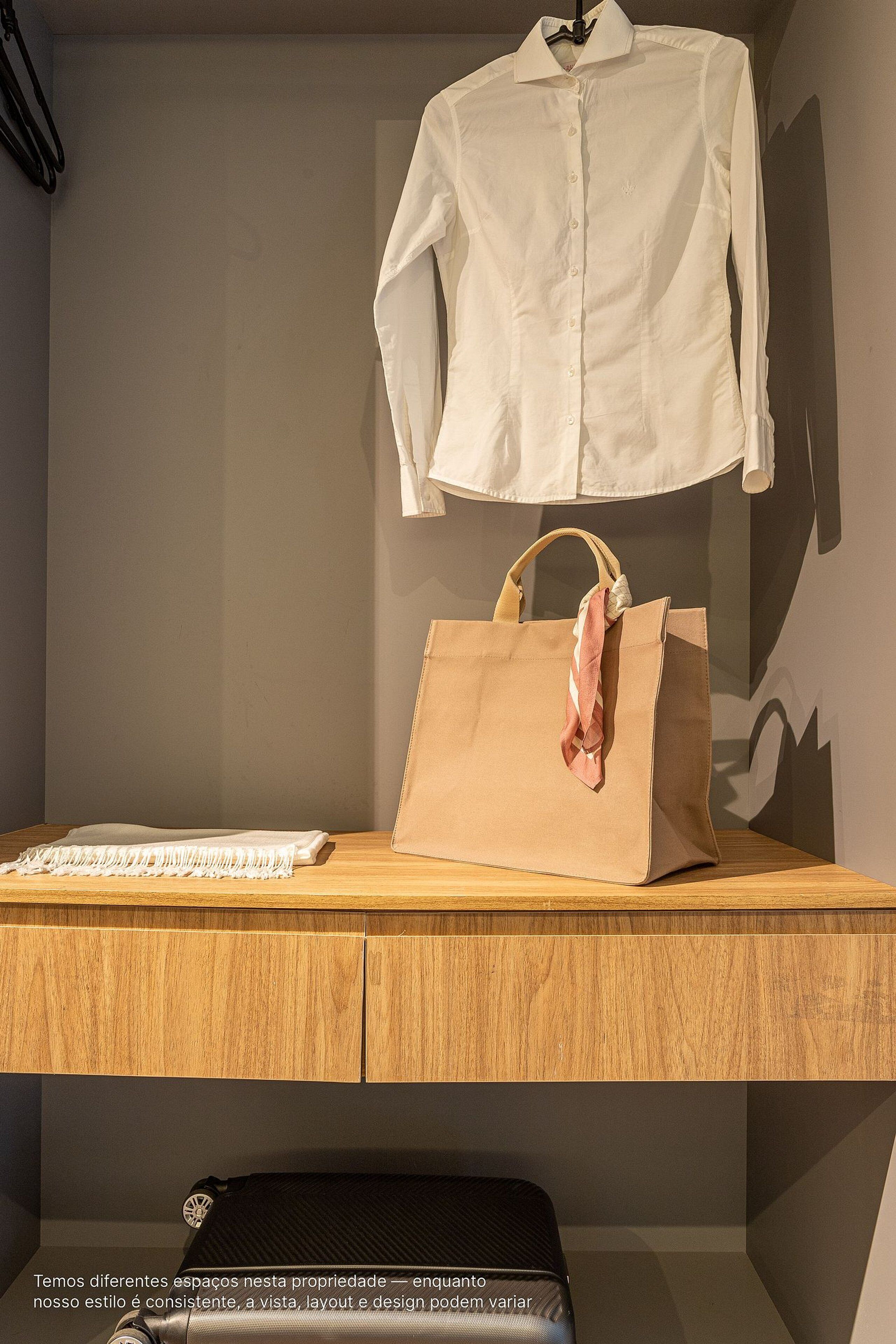 Une pièce avec un bureau en bois, une chemise blanche suspendue, un sac en papier brun et un sac noir.