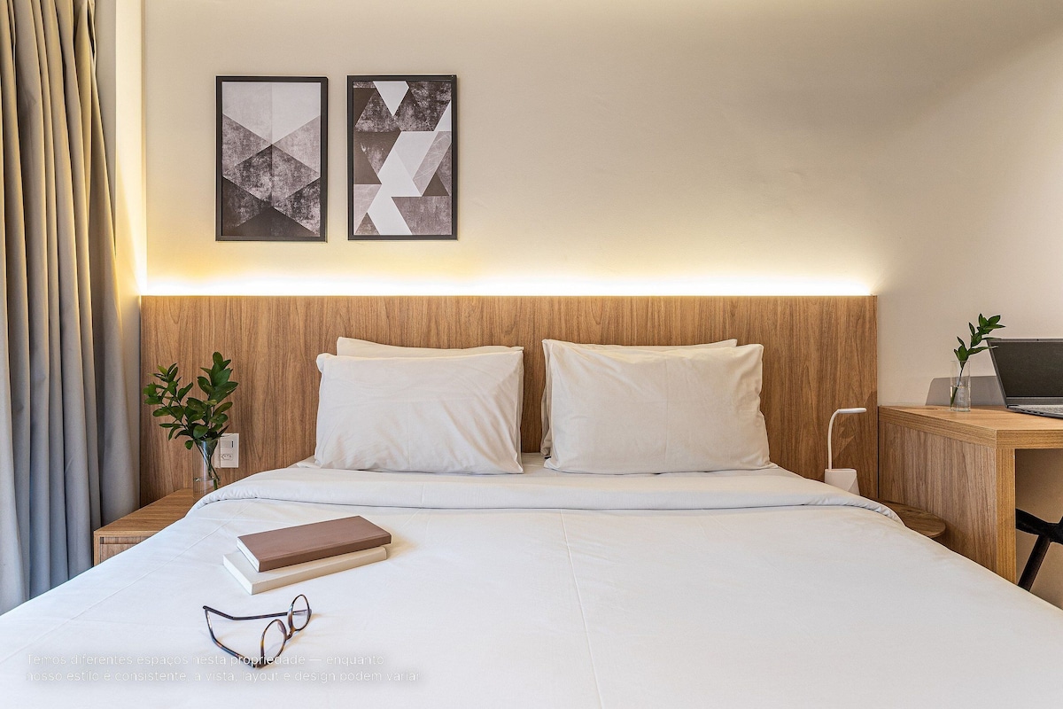 A neatly made bed with white linens, a bedside table with a laptop, and two abstract paintings on the wall.