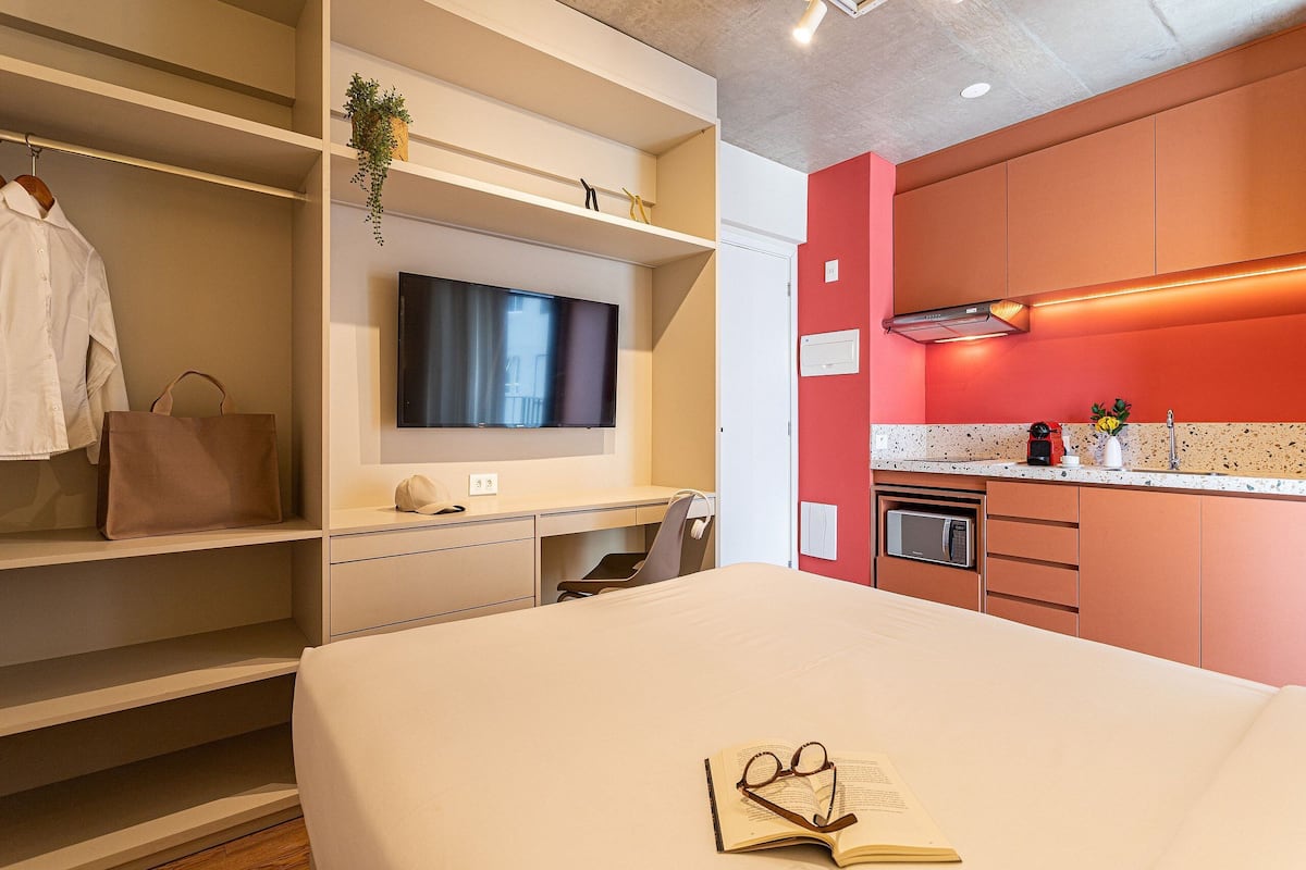 Une chambre d’hôtel équipée d’un lit, d’une télévision, d’un bureau, d’un four à micro-ondes et d’un mur d’accent de couleur rouge.