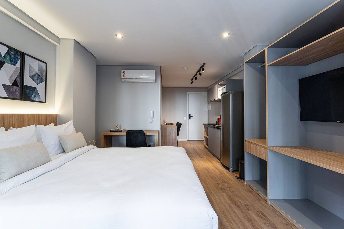 Une chambre d’hôtel moderne dotée d’un grand lit, d’un bureau, d’une kitchenette et d’un téléviseur fixé au mur.