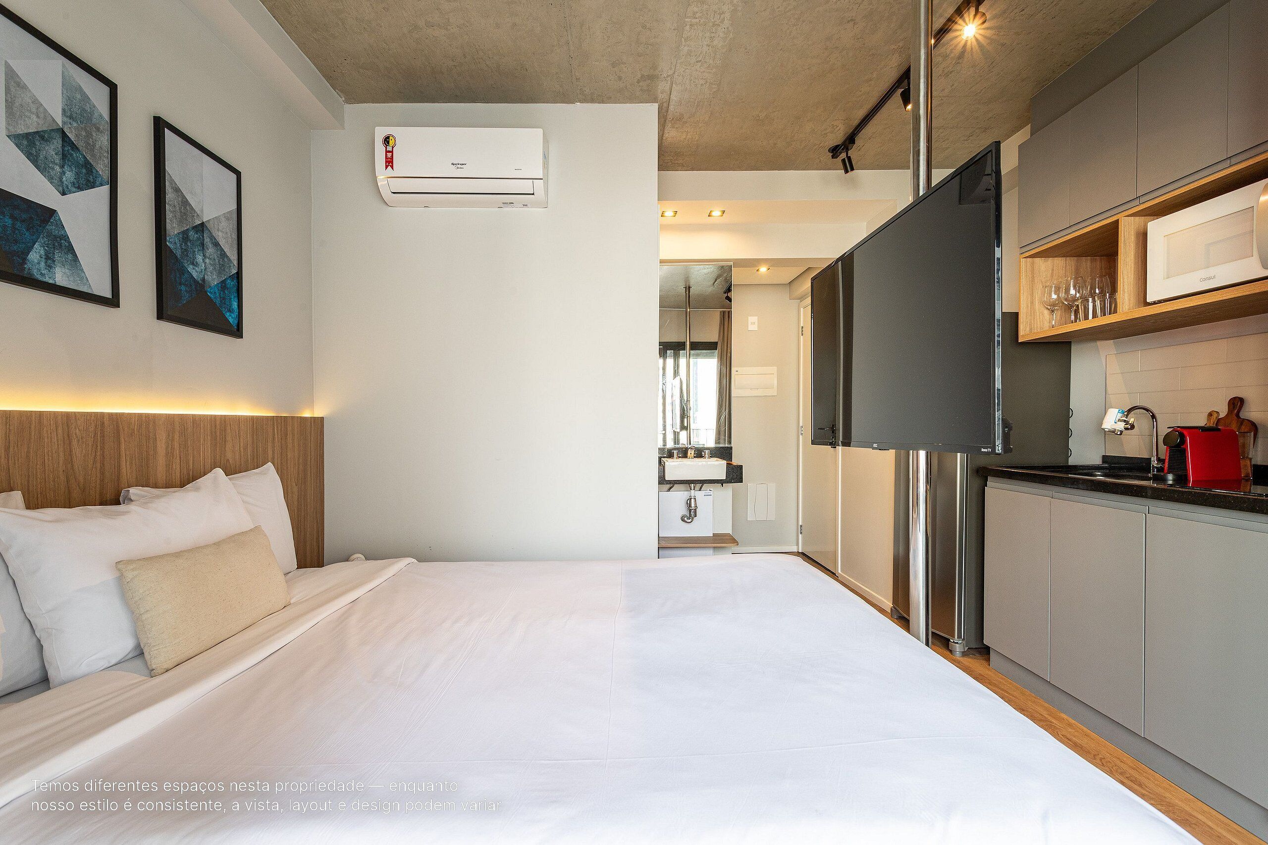 Een moderne hotelkamer met een groot bed, een kitchenette en een badkamer op de achtergrond.