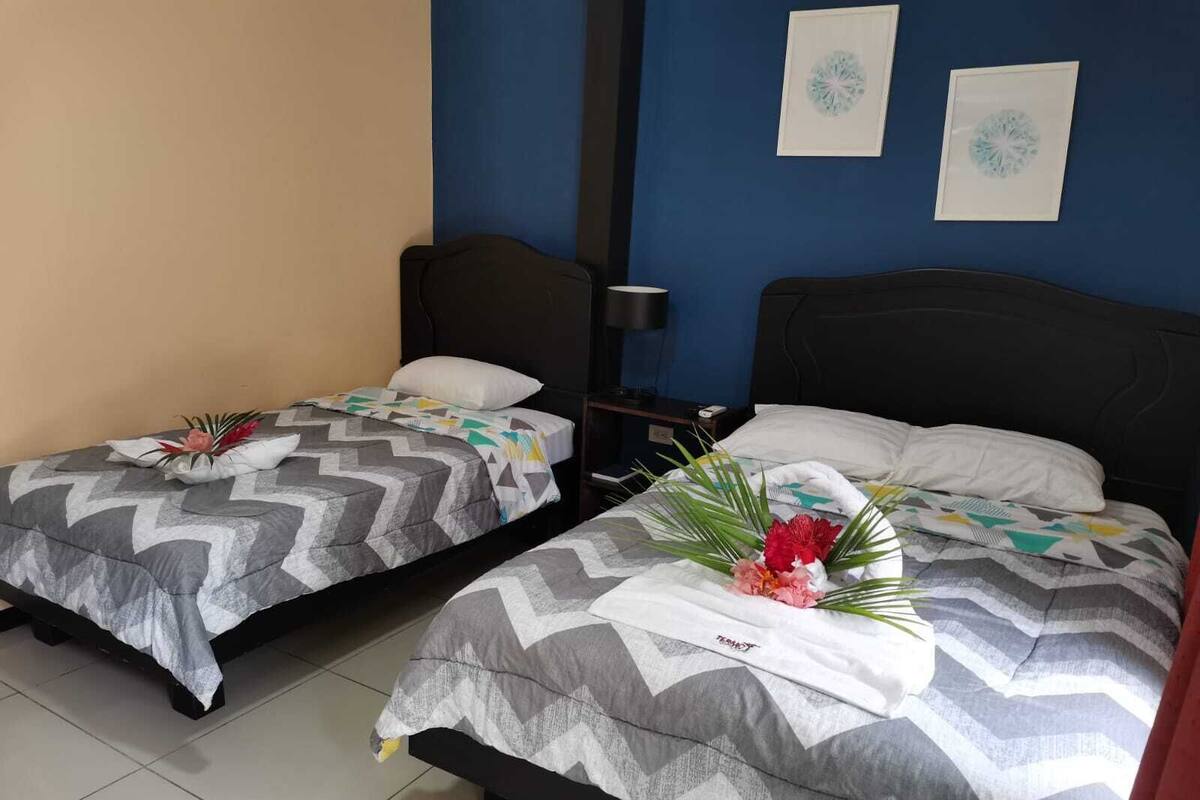 Two single beds with geometric-patterned bedding, a nightstand with a lamp, and two framed wall art pieces.