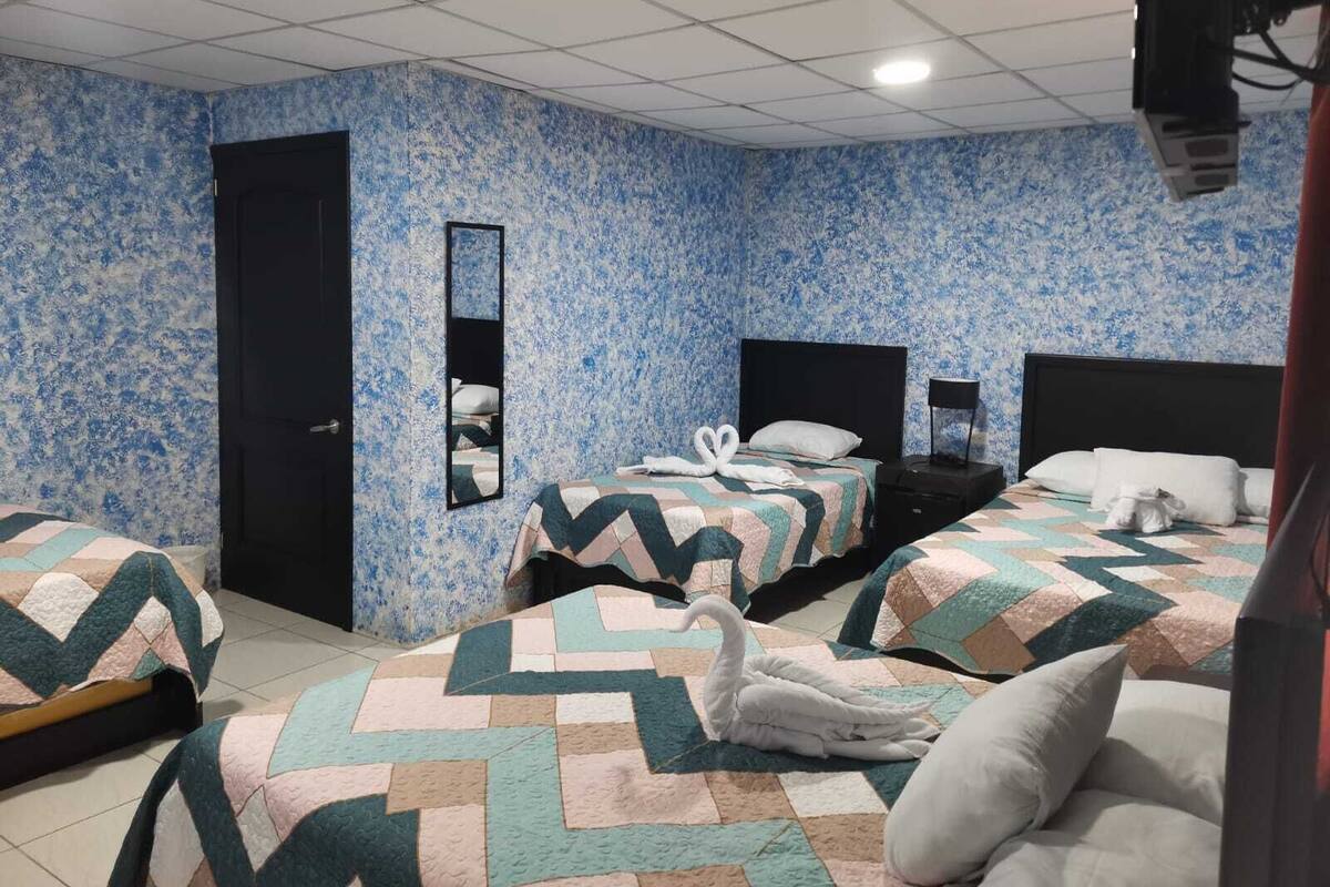 A hotel room with three beds, a large mirror, and a patterned wall.