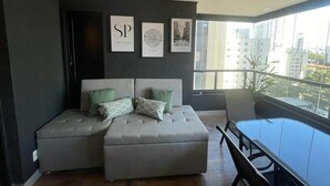 A modern living room with a grey sofa, a dining table, and artwork on the wall. - Ator - Chic Studio in Vila Olimpia (São Paulo)
