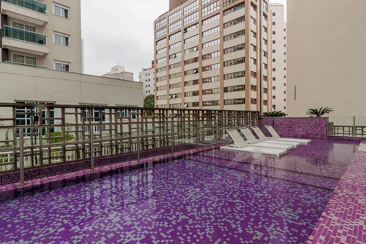 Una piscina en la azotea con suelo de baldosas moradas, rodeada por una barandilla de cristal y sillas de descanso.