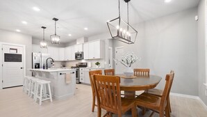 Una cocina moderna con armarios blancos, una isla central con taburetes e iluminación colgante.