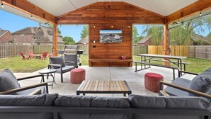 Un patio al aire libre con vigas de madera, un televisor montado en la pared y vistas de un vecindario.