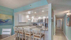 Cocina moderna con armarios blancos, una isla central con taburetes y electrodomésticos como microondas y tostadora.