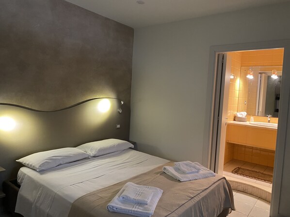 A hotel room with a bed, a nightstand, a wall-mounted light, and a bathroom visible through an open door.