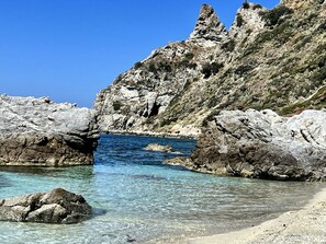 A rocky coastal landscape with clear blue waters and a natural rock formation.