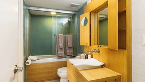 A bathroom with a shower, toilet, sink, and wooden cabinets. - Captain's Quarters | Top Floor | Ocean Pointe 4405 (Tavernier)