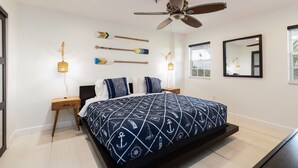 A bedroom with a bed, two nightstands, a ceiling fan, a wall-mounted mirror, and a window with a view of the outdoors. - Captains Quarters Ocean Pointe 4405 (Tavernier)