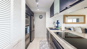 A modern kitchen with stainless steel appliances, a marble countertop, and a large mirror above the sink. - Captains Quarters Ocean Pointe 4405 (Tavernier)