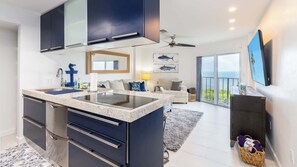 A modern kitchen with dark cabinetry, a central island, and a large window overlooking the sea. - Captain's Quarters | Top Floor | Ocean Pointe 4405 (Tavernier)