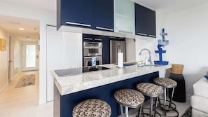 Cozinha moderna com armários azul escuro, eletrodomésticos de aço inoxidável, bancada de mármore e espaço para banquetas.