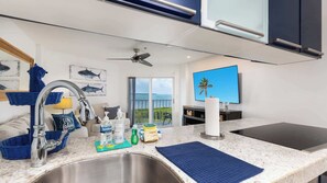 A modern kitchen with a stainless steel sink, a ceiling fan, and a view of the ocean through large windows. - Captains Quarters Ocean Pointe 4405 (Tavernier)
