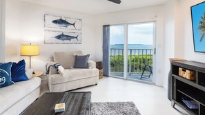 A living room with a sofa, a coffee table, and a fireplace. There is a balcony with a view of the sea. - Captain's Quarters | Top Floor | Ocean Pointe 4405 (Tavernier)