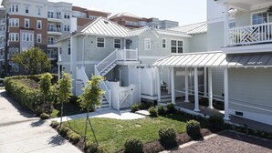 A two-story residential building with a covered porch, a staircase, and a small front yard with landscaping. - Cape Henry Full Suite Inn at Old Beach (Virginia Beach)