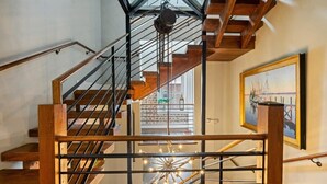 Una escalera de madera con barandillas metálicas que conduce a una habitación con un ventanal y un cuadro en la pared.