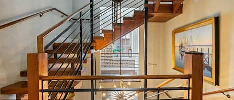 Una escalera de madera con barandillas metálicas que conduce a una habitación con un ventanal y un cuadro en la pared.