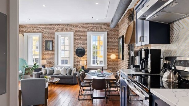 Una cocina moderna con pared de ladrillo, un comedor con mesa y sillas, y un sofá al fondo.