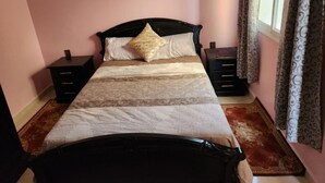 Een bed met hoofdbord, twee nachtkastjes en een raam met gordijnen.