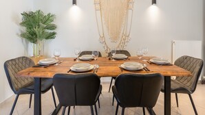 Un comedor con una mesa de madera dispuesta para seis personas, sillas negras y un colgador de macramé en la pared.
