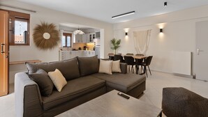 Una sala moderna con un sofá modular, una mesa de comedor con sillas y una cocina al fondo.