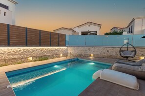Une piscine bordée d’un muret en pierre, entourée d’une clôture en bois, et agrémentée d’un fauteuil suspendu.
