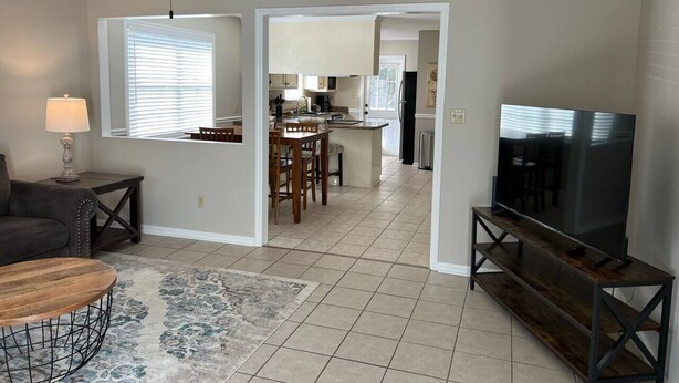 A living room with a sofa, coffee table, TV, and kitchen in the background. - Get-Away on Wayland Cozy Cottage (Valdosta)