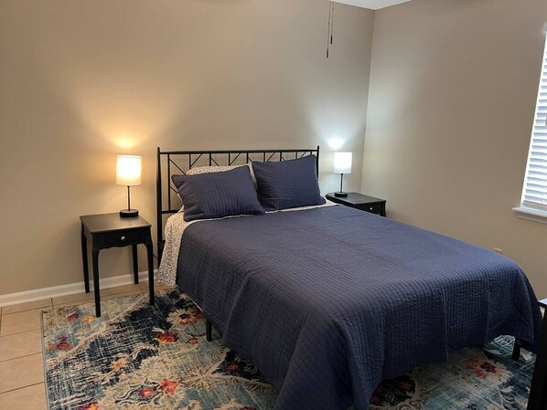 A bedroom with a bed, two bedside tables, and a nightstand. - Get-Away on Wayland Cozy Cottage (Valdosta)