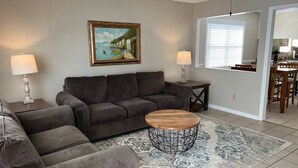 A living room with a gray sofa, a coffee table, and a painting on the wall. - Get-Away on Wayland Cozy Cottage (Valdosta)