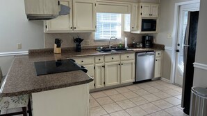 A kitchen with white cabinets, a granite countertop, a dishwasher, and a microwave. - Get-Away on Wayland Cozy Cottage (Valdosta)
