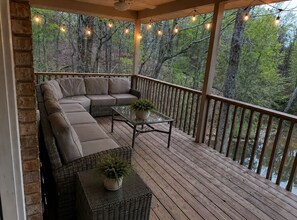 Une terrasse extérieure couverte, aménagée avec un canapé modulable, une table en verre et des plantes en pot.