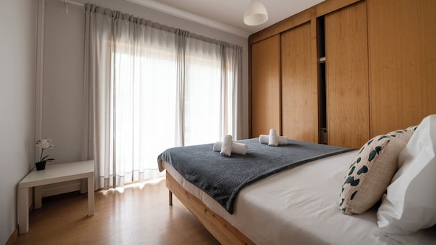 Une chambre à coucher avec un lit, un banc, une plante en pot et une fenêtre avec des rideaux.