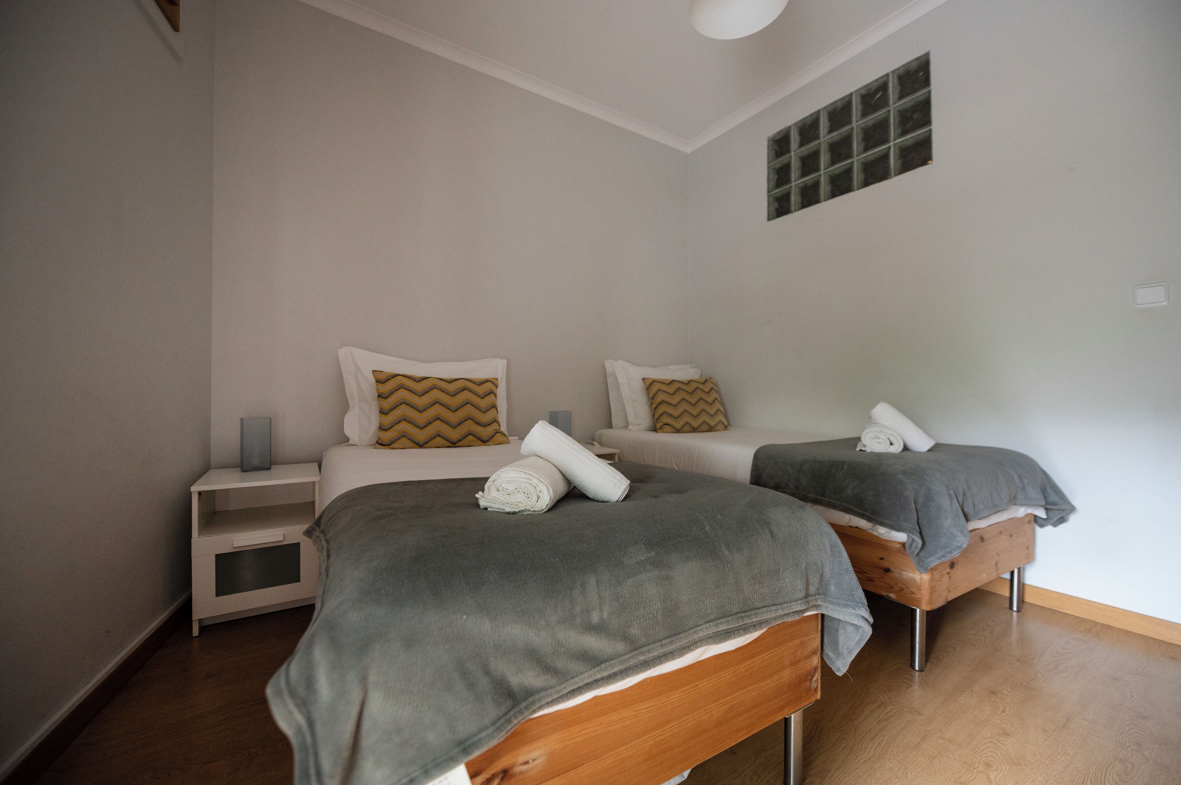 A bedroom with two beds, a nightstand, a small shelf, and a window with a view.
