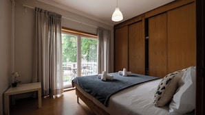 Une chambre avec un lit, un banc, une plante en pot et une vue sur l’extérieur.