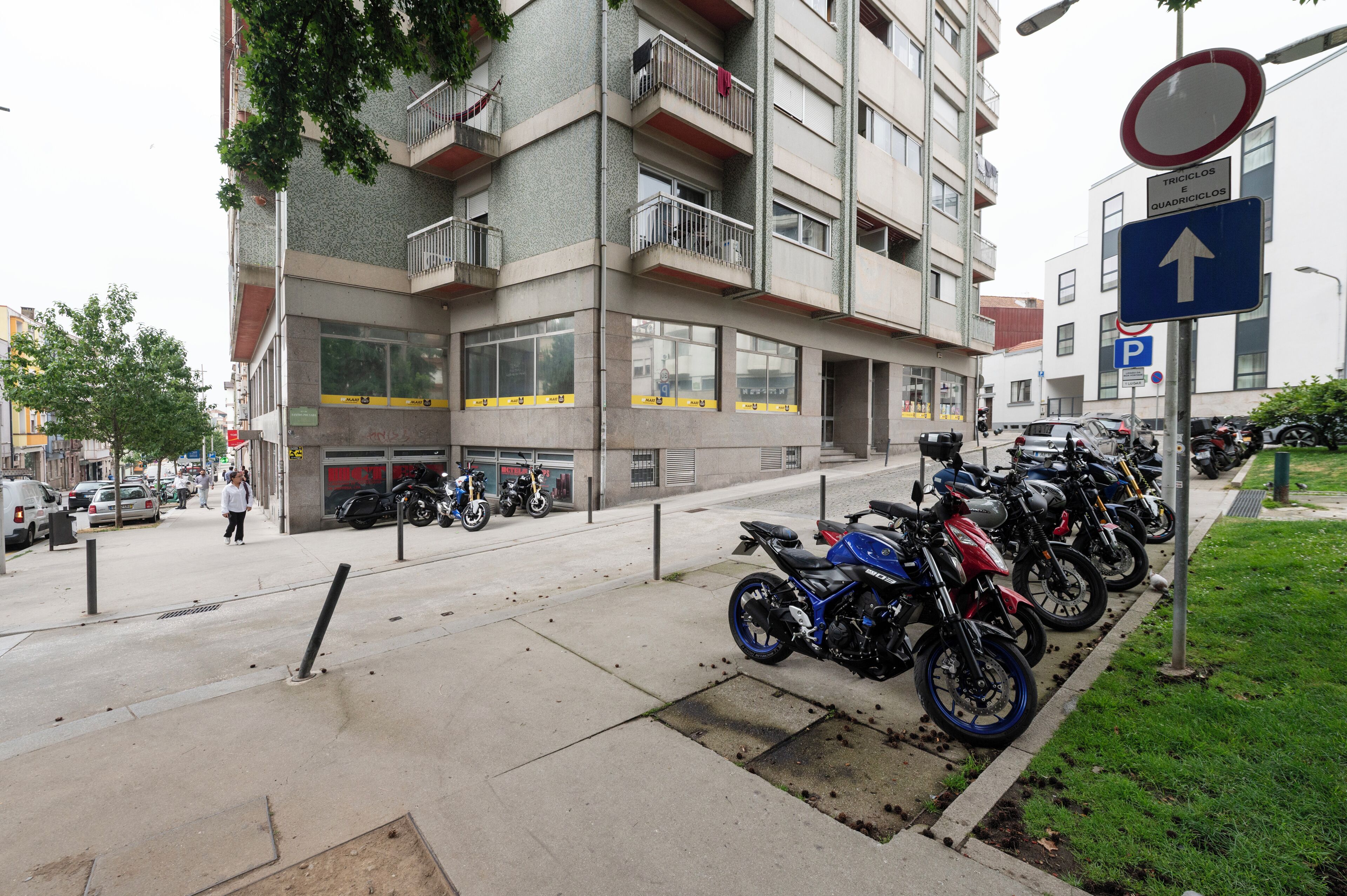 Un edificio de varios pisos con balcones, una fila de motocicletas estacionadas y un paso para peatones.