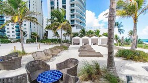 Eine Strandlounge mit Korbmöbeln, einem blau gefliesten Tisch und Palmen.